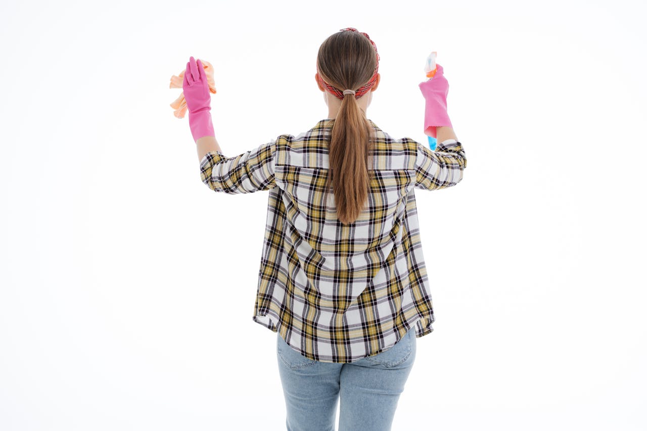 hero-img-02 Back view of a woman in latex gloves cleaning with spray and cloth, indoor studio shot.